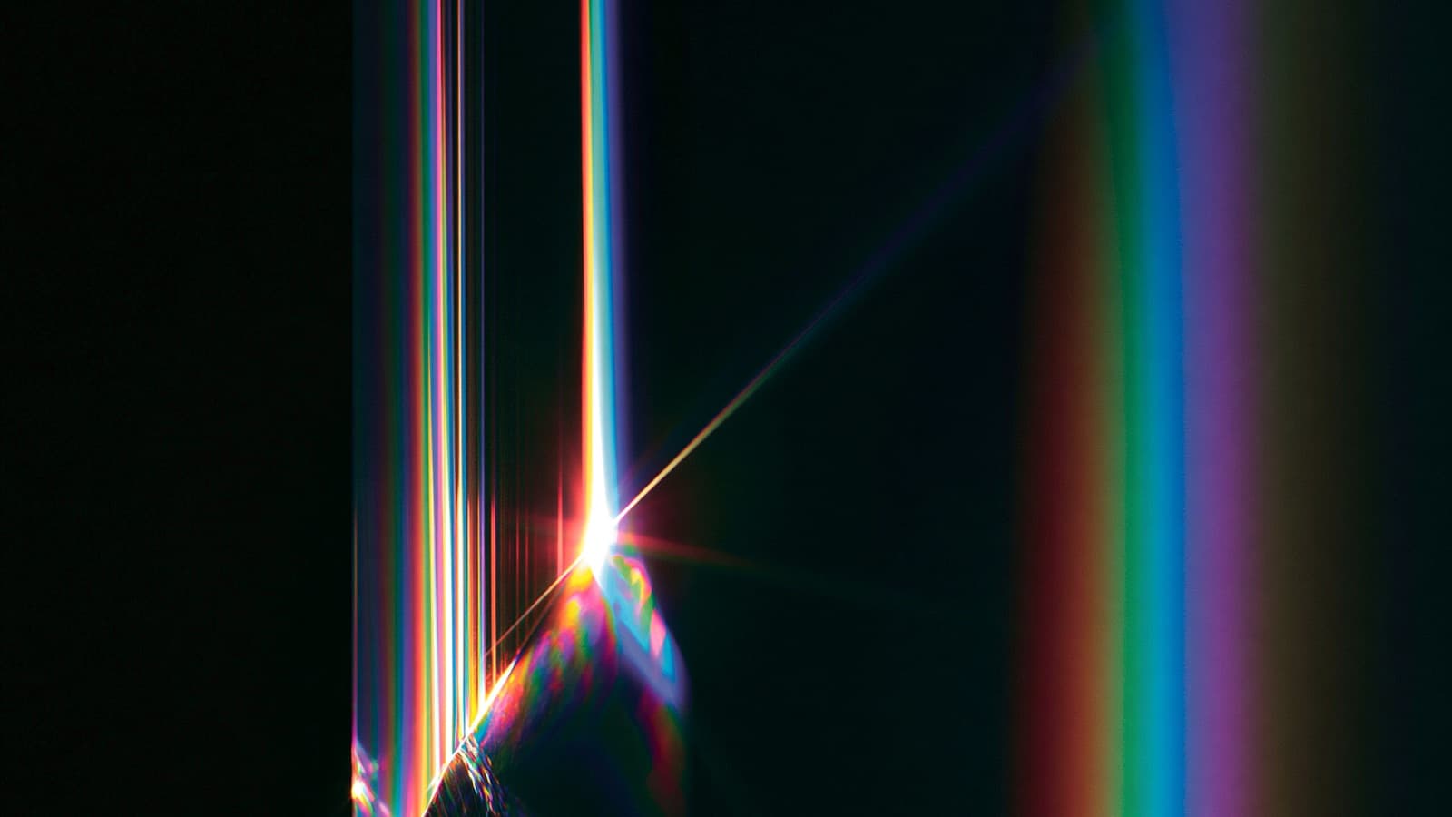 A beam striking the edge of a prism and throwing one hard rainbow band.
